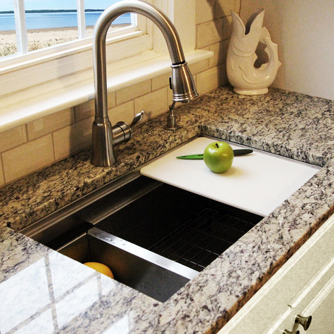 A kitchen sink with an apple on the cutting board.